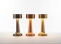 Trois lampes nomades LUMORA Lueur en métal brossé, finitions argent, cuivre et or, design tactile sans fil.