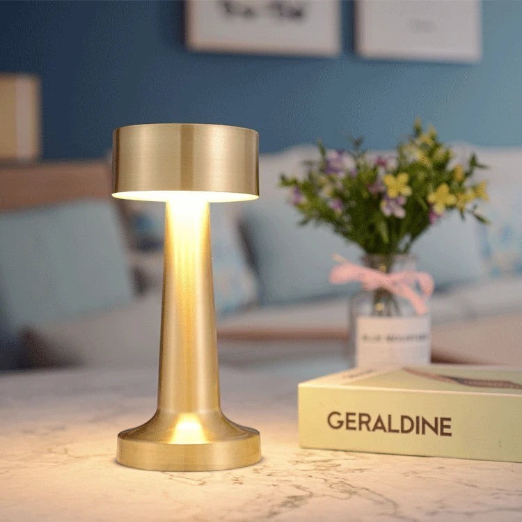 Lampe nomade LUMORA Lueur en métal doré, sans fil et tactile, diffusant une lumière blanc chaud sur une table